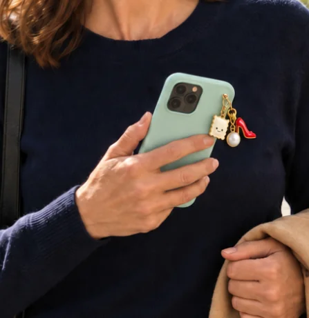 La raviole en charm doré accrochée à un smartphone vert, tenu en main